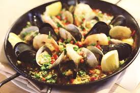 A skillet of clams with herbs and lemon wedges.