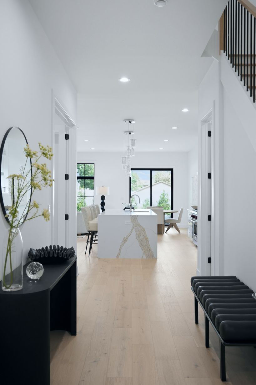 Modern white kitchen with a veined-stone island, light wood floors, and black-framed windows.
