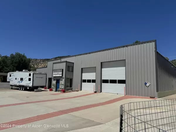 Gray metal commercial building with two garage doors, a travel trailer, and a paved lot.