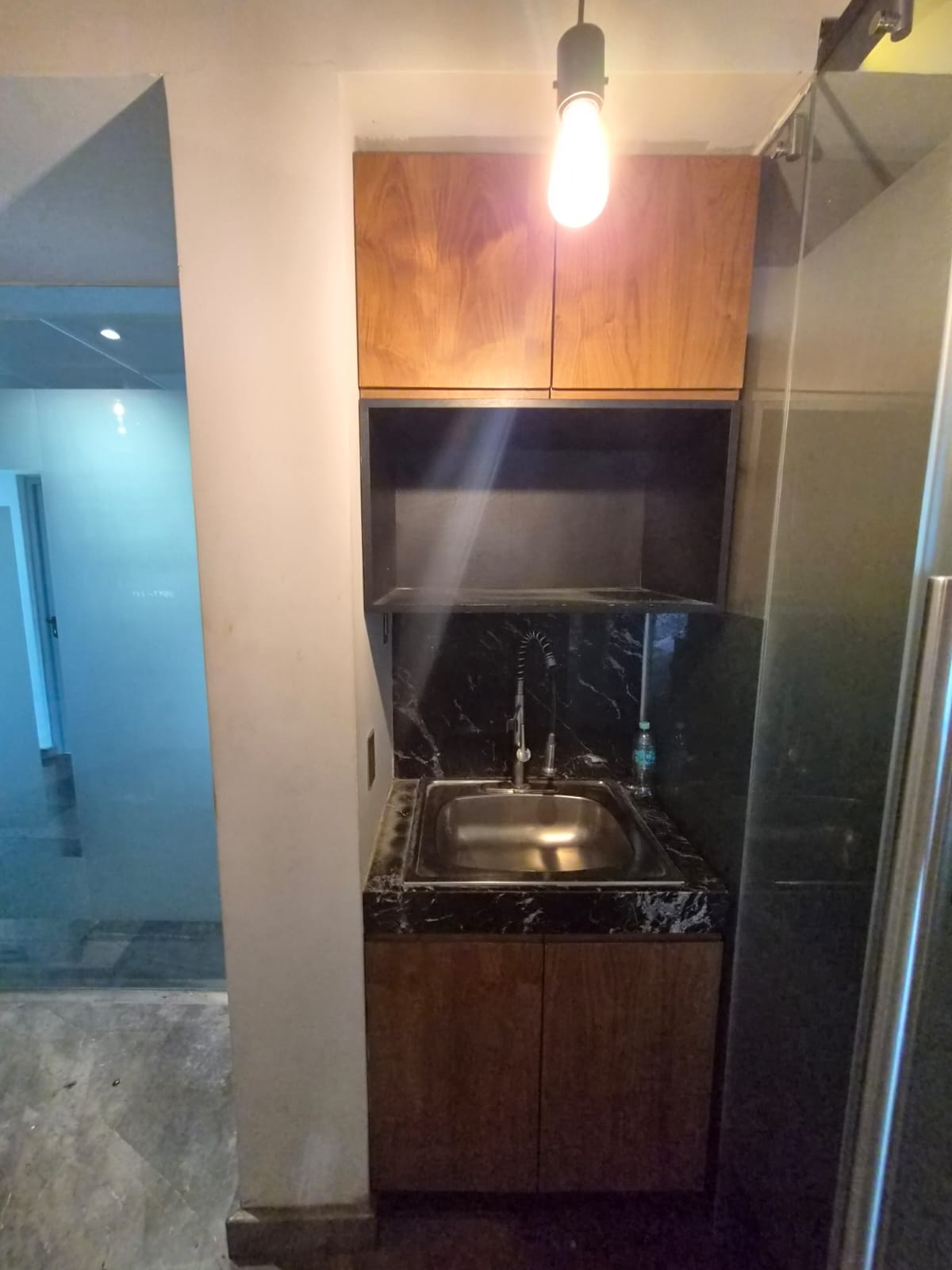 Compact office kitchenette with a stainless-steel sink, dark stone counter, and wood cabinets.