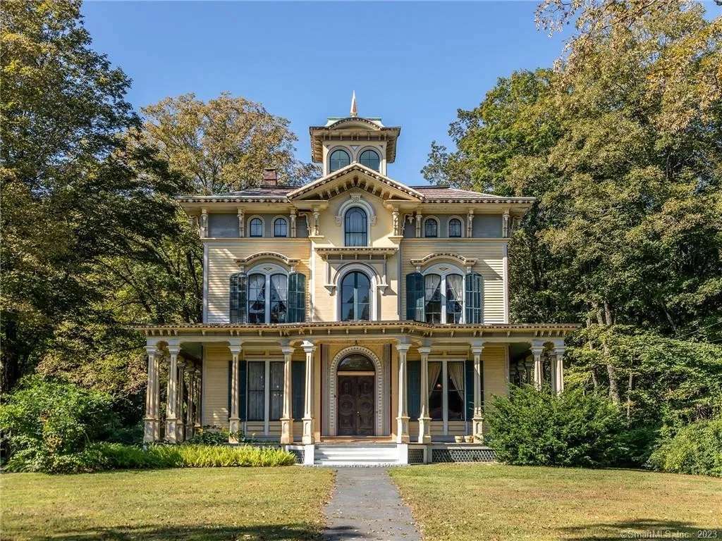 Historic yellow Victorian-style house with ornate trim, central tower, and a tree-lined front lawn.