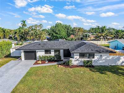Modern single-story home with a wide driveway, front lawn, and tropical landscaping.