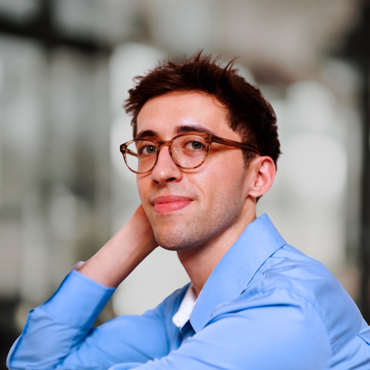 Benjamin Anderson in amber glasses and a blue shirt, resting one hand behind his neck.