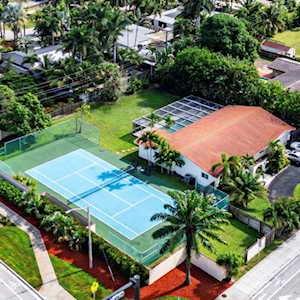 Aerial view of two tennis courts beside a low building and palm trees.