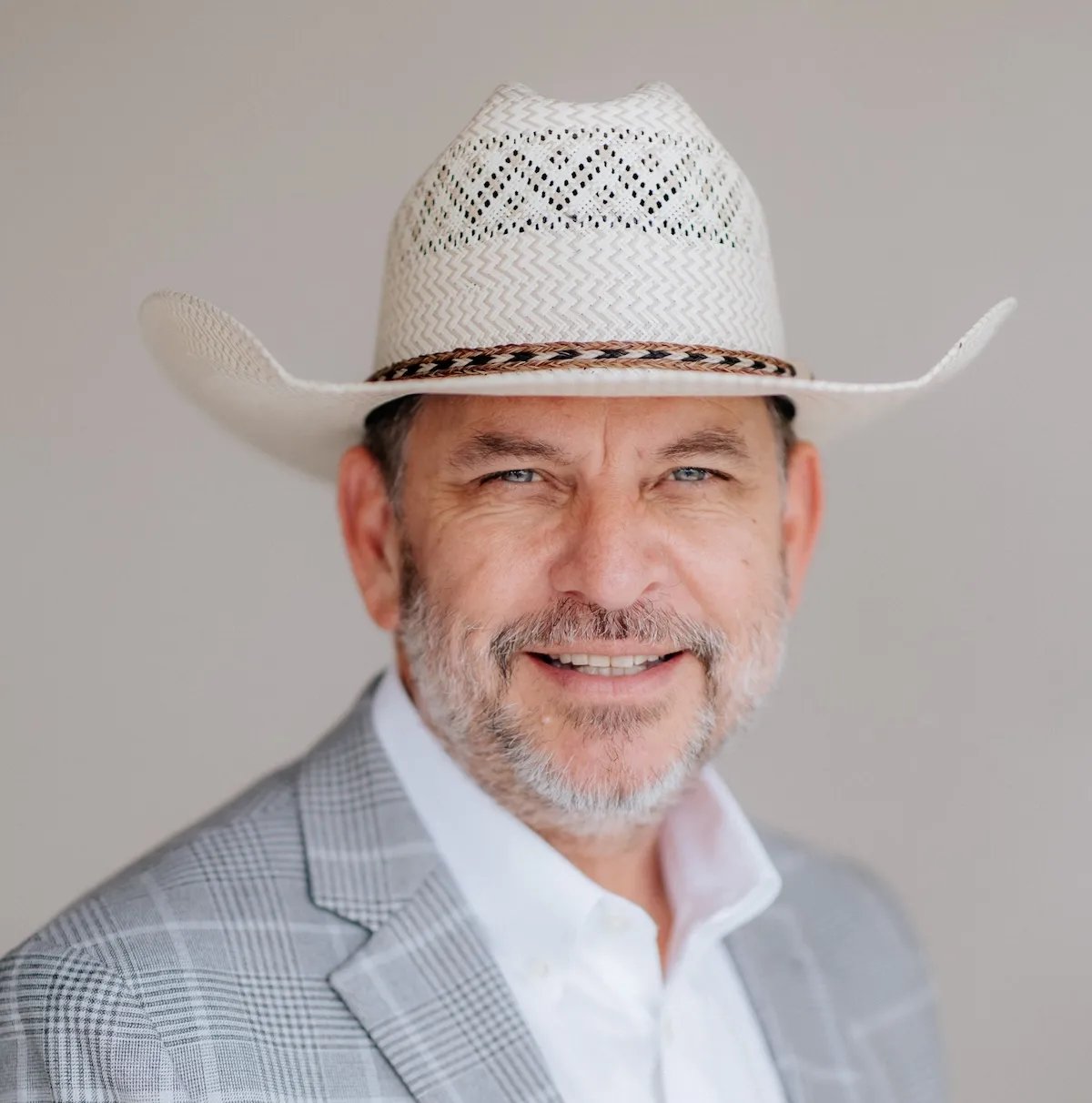 Smiling man in a white cowboy hat and gray plaid blazer.