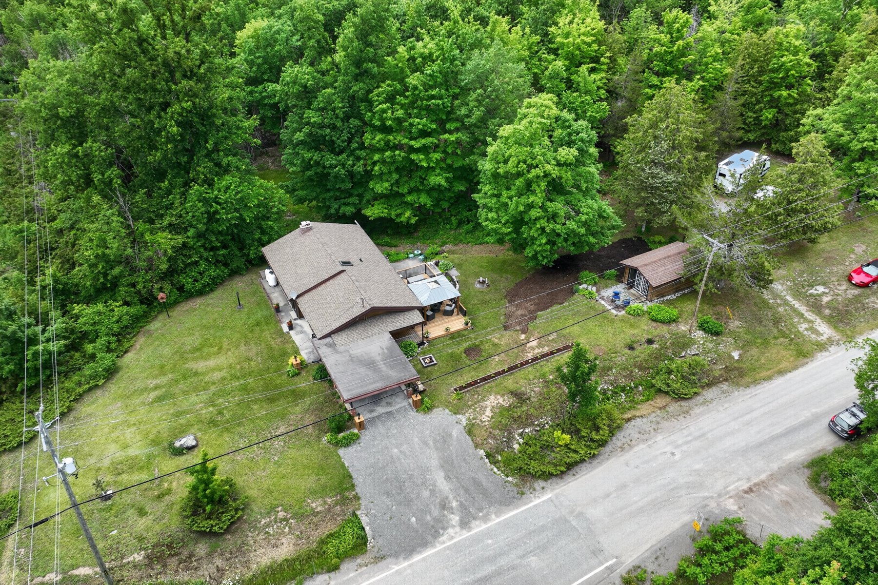 Aerial view of a home and detached outbuilding on a wooded lot beside the road.