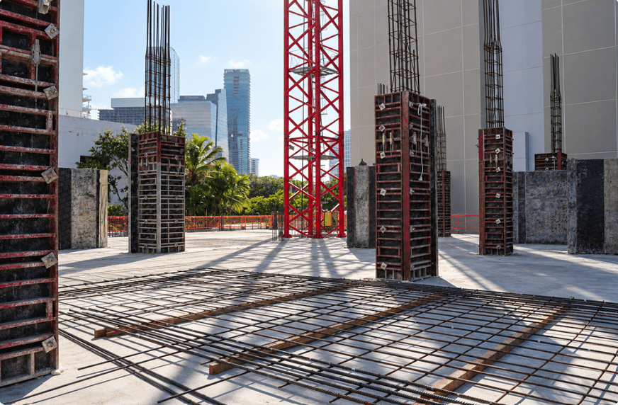 Condominium construction site with exposed rebar, concrete columns, and a red tower crane.