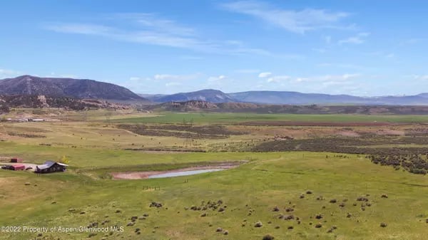 Open fields and a pond stretch toward mountain ranges near Meeker, Colorado.
