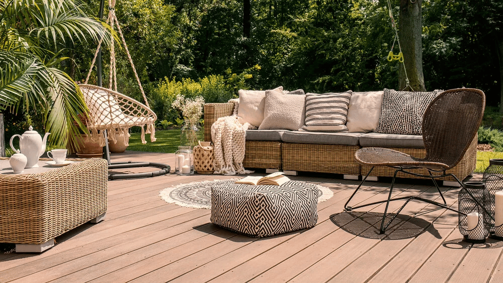 Outdoor patio with wicker seating, a hanging chair, and a lush garden backdrop.