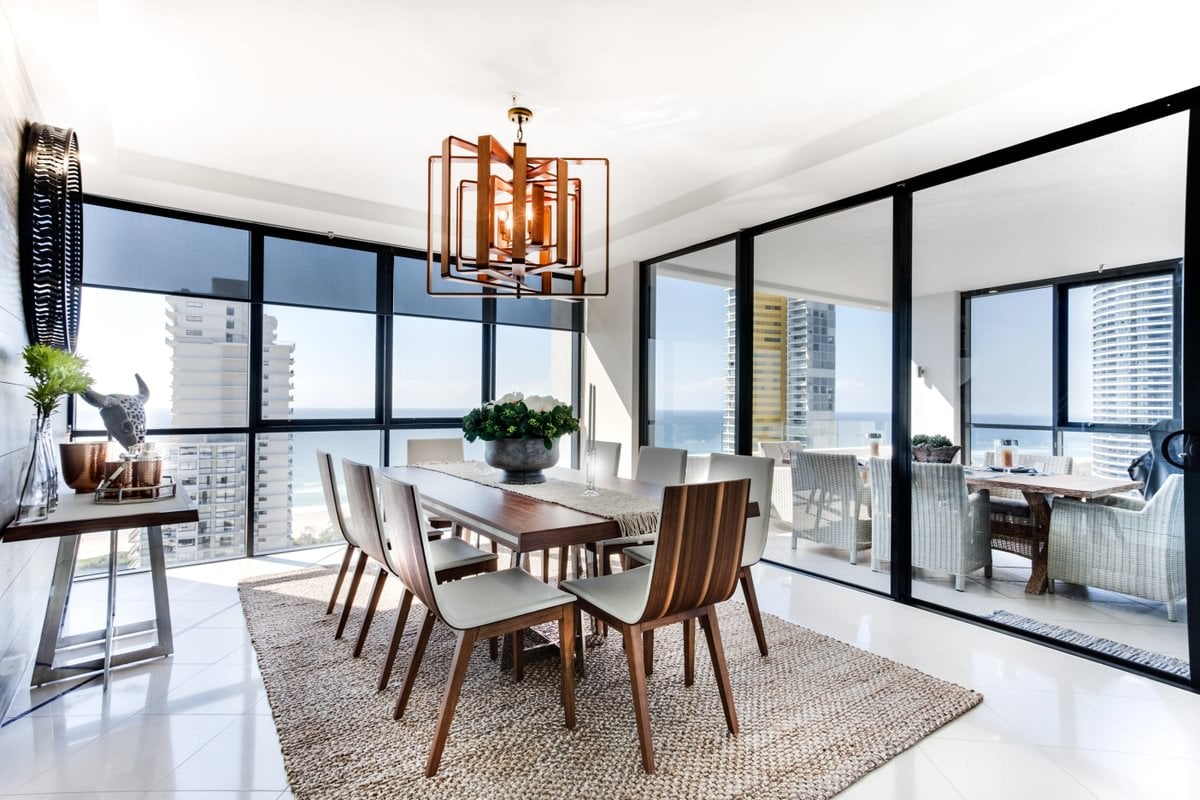 High-rise dining room with a wood table, geometric pendant light, and floor-to-ceiling windows overlooking water.