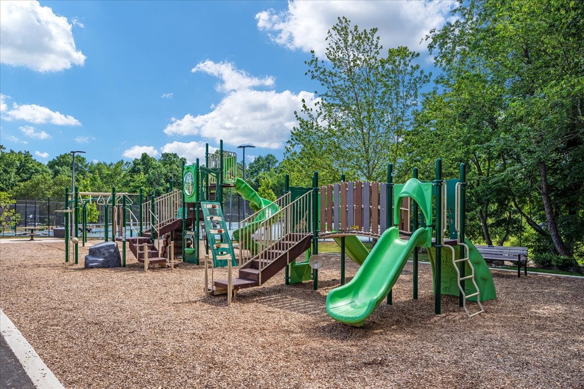 Community playground with green slides and climbing structures on a wood-chip surface.