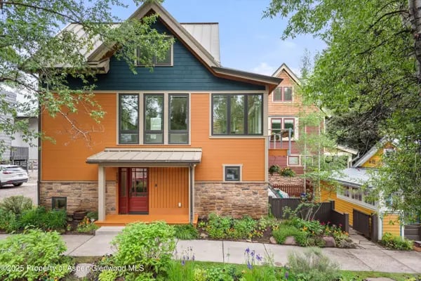 Aspen home with orange siding, dark blue gables, stone veneer, and leafy trees.