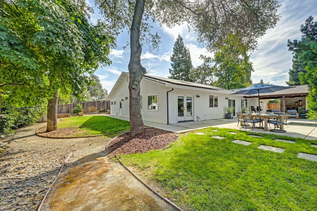 Single-story home with a covered patio and outdoor dining area beneath mature trees.