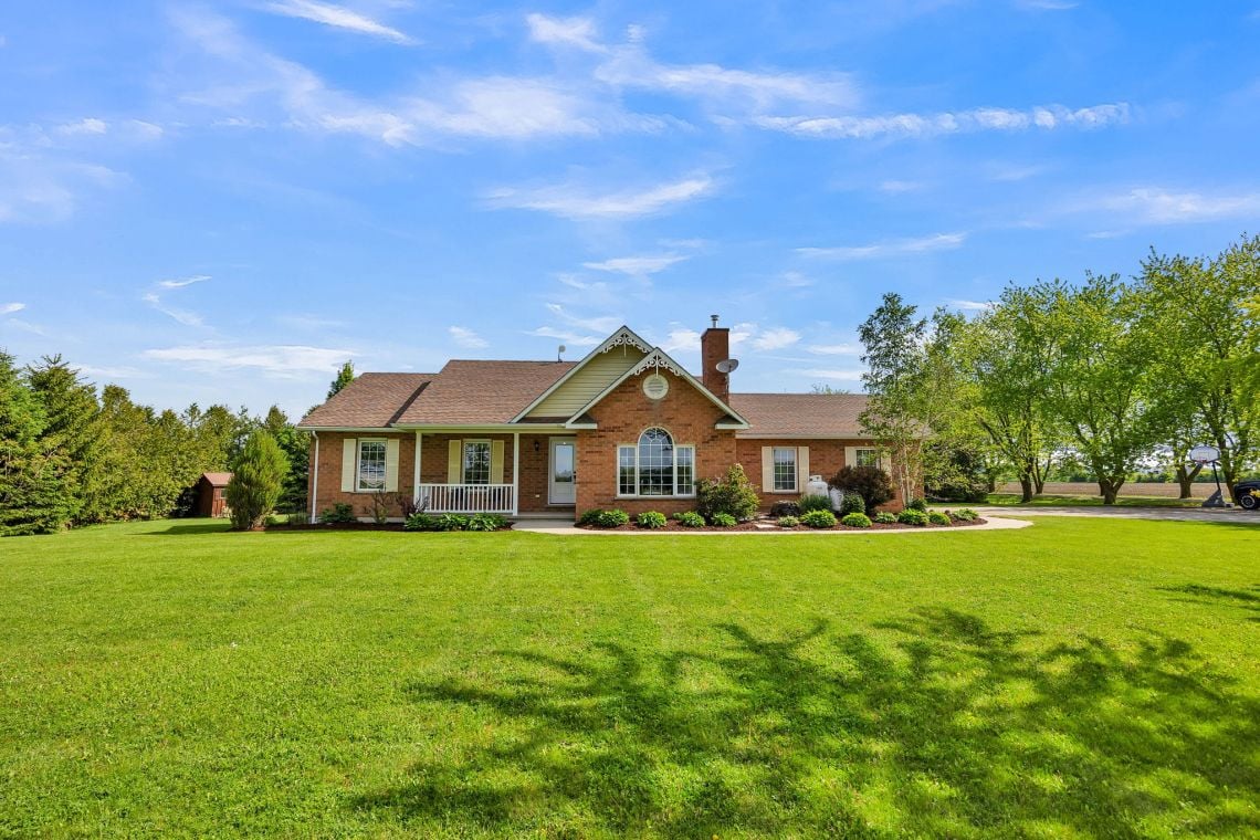 Red brick house with a front gable and arched window behind a broad green lawn.