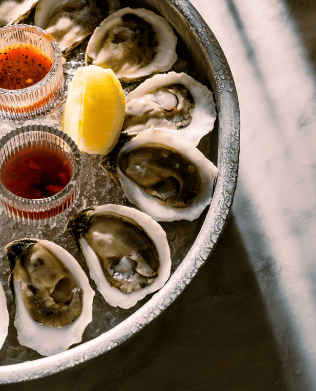Oysters on the half shell with sauces and a lemon wedge on a chilled platter.