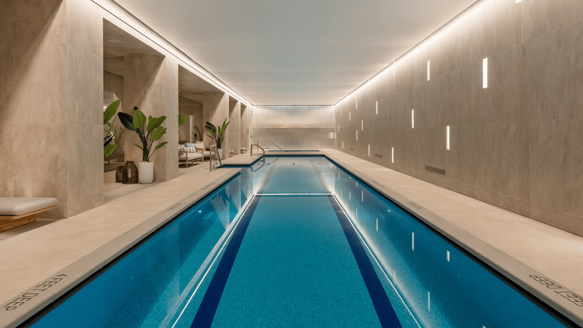 Indoor swimming pool with blue water, pale stone walls, and a lounge seating area.