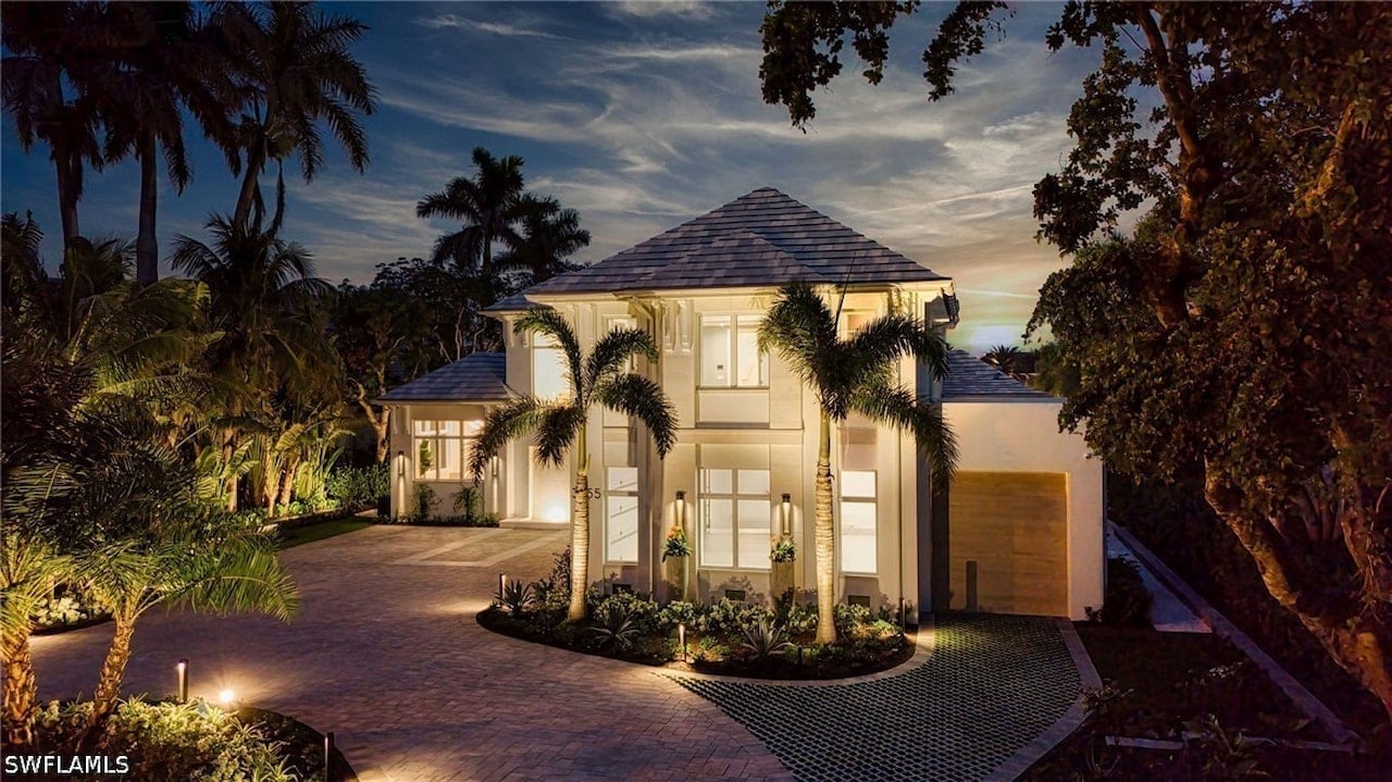 Modern white two-story home with a paved driveway and palm trees at dusk.