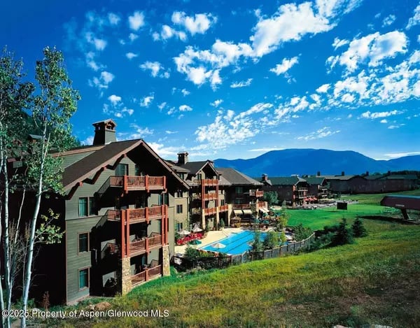Mountain-style condominiums with balconies and a pool, backed by mountains.