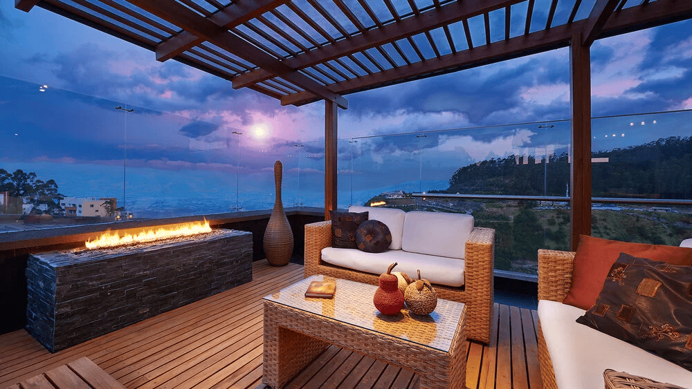Furnished terrace with a pergola, lit fireplace, and ocean views at dusk.
