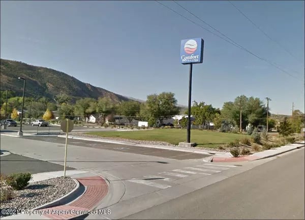 Rifle street corner with a crosswalk and Comfort sign, backed by foothills.