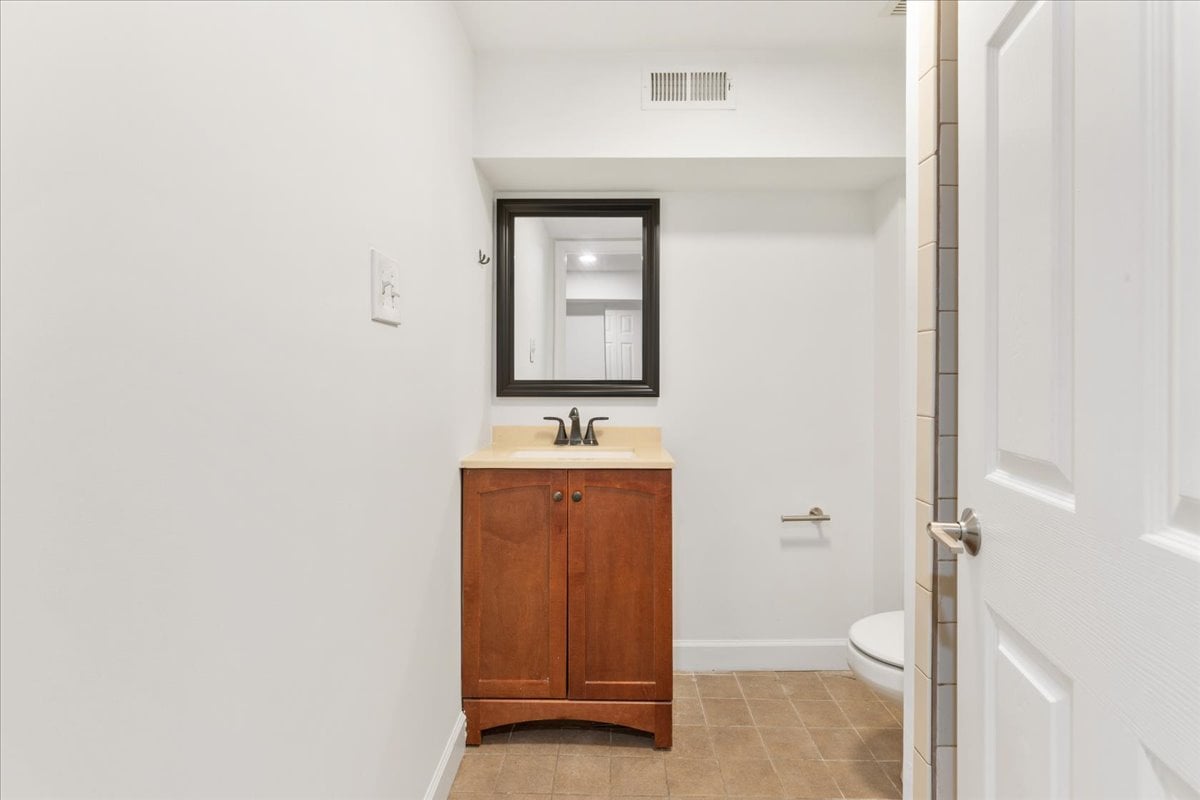 Bathroom with a reddish wood vanity, dark-framed mirror, and brown tile floor.