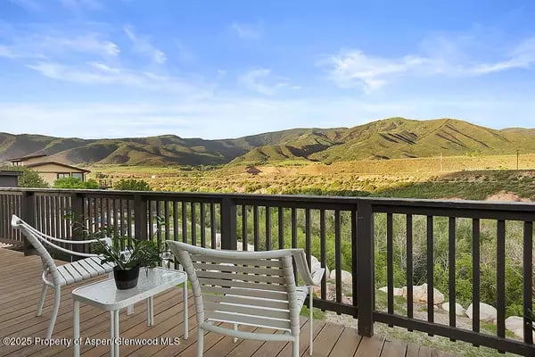 Deck with patio chairs overlooking sunlit mountain ridges.