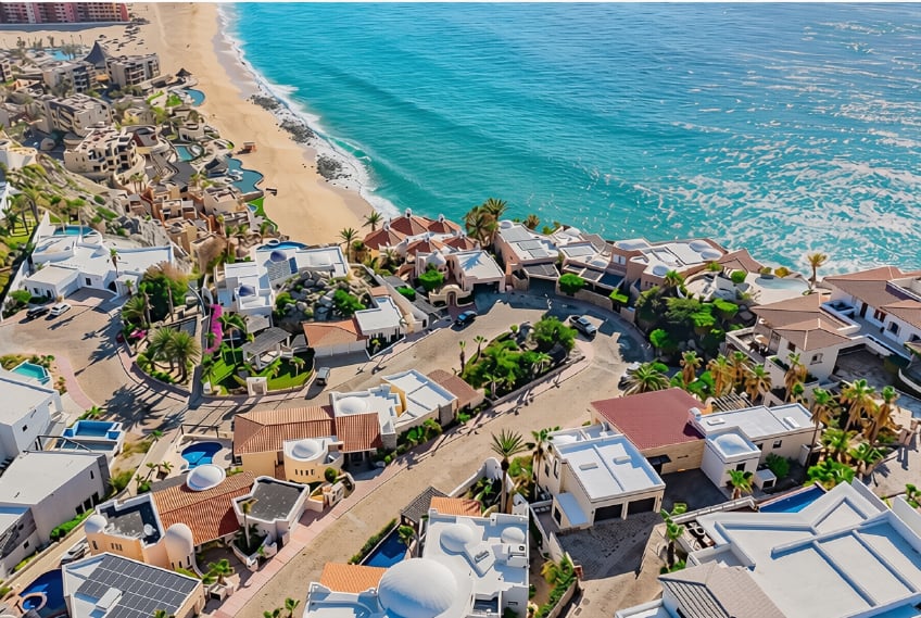 Coastal homes beside a sandy beach and turquoise ocean, viewed from above.