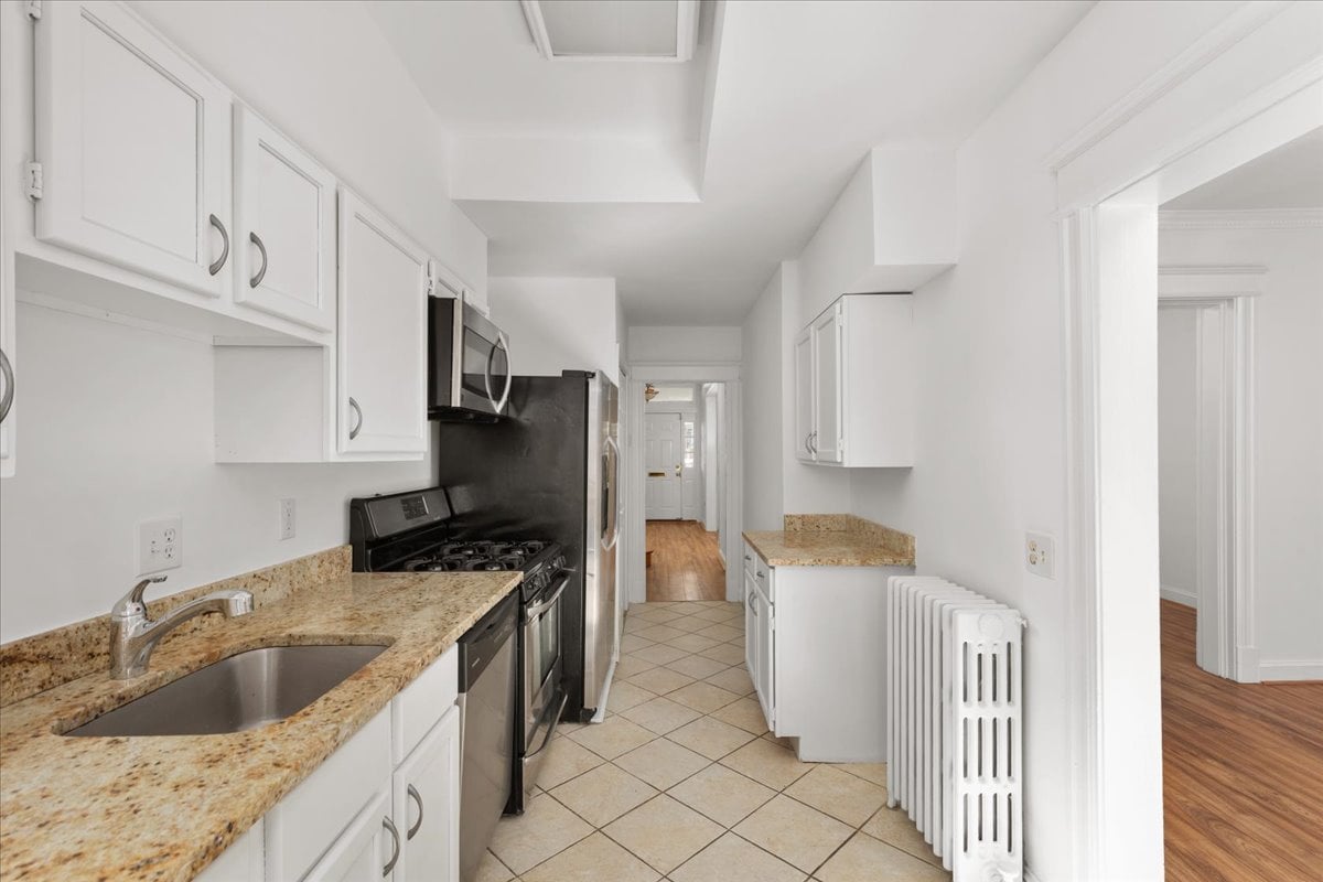 Galley kitchen with granite counters, white cabinets, stainless steel appliances, and a radiator by the doorway.
