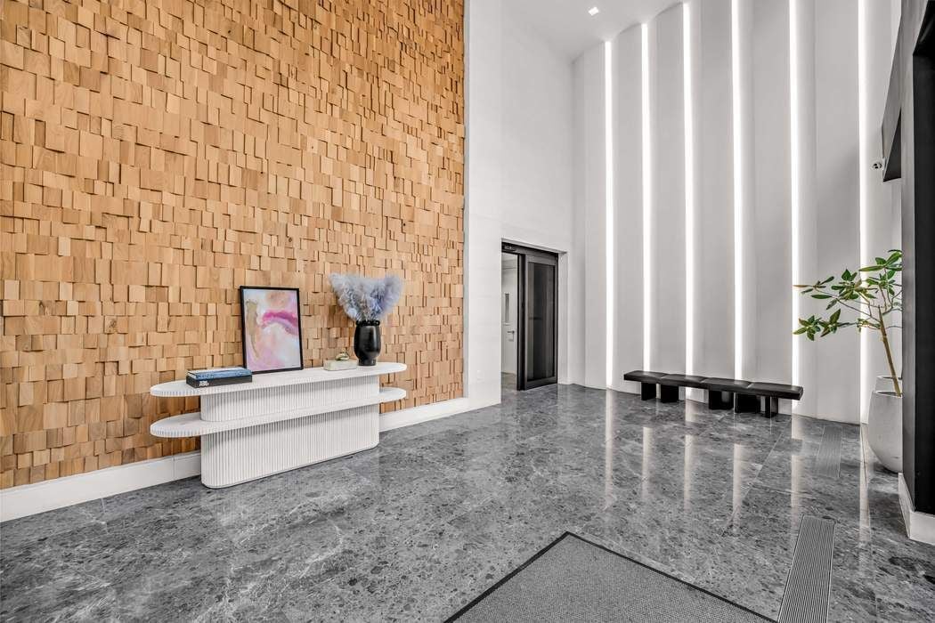 Modern lobby with a textured wood wall, polished stone floor, and tall illuminated panels.