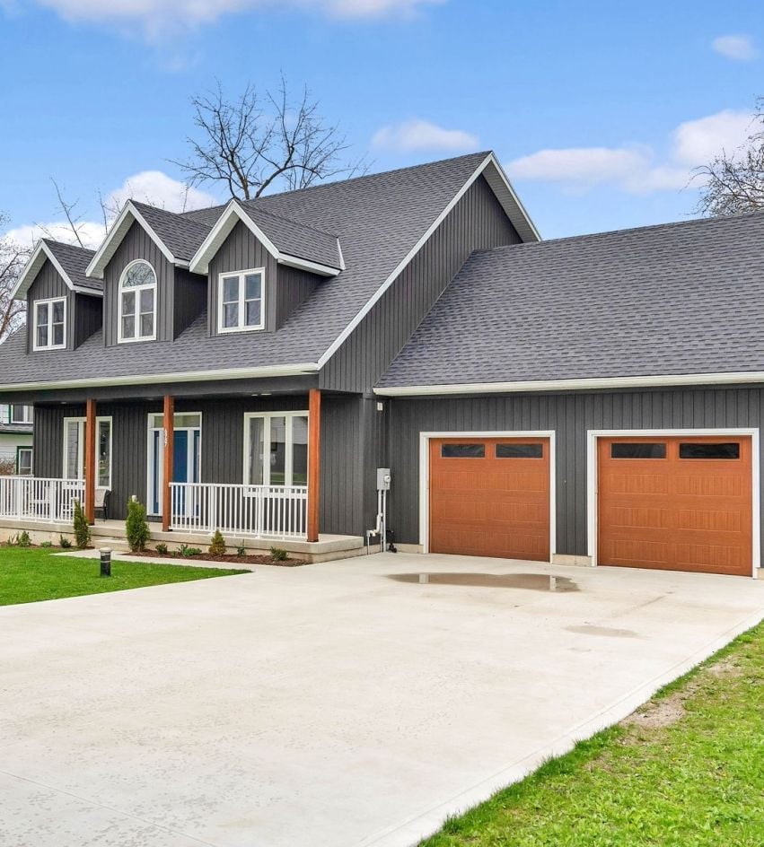 Charcoal-gray two-story home with roof dormers, a covered porch, and two orange-brown garage doors.