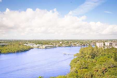 A broad waterway curves past green shoreline vegetation and waterfront buildings.
