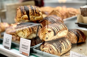 Chocolate-drizzled pastries displayed on trays in a bakery case.