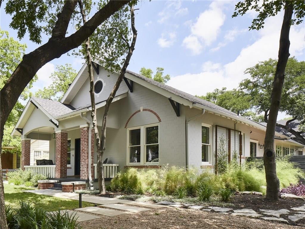 Side elevation of a craftsman-style 1932 home in Pemberton Heights on Northwood Road in Austin, Texas, framed by mature oak trees.