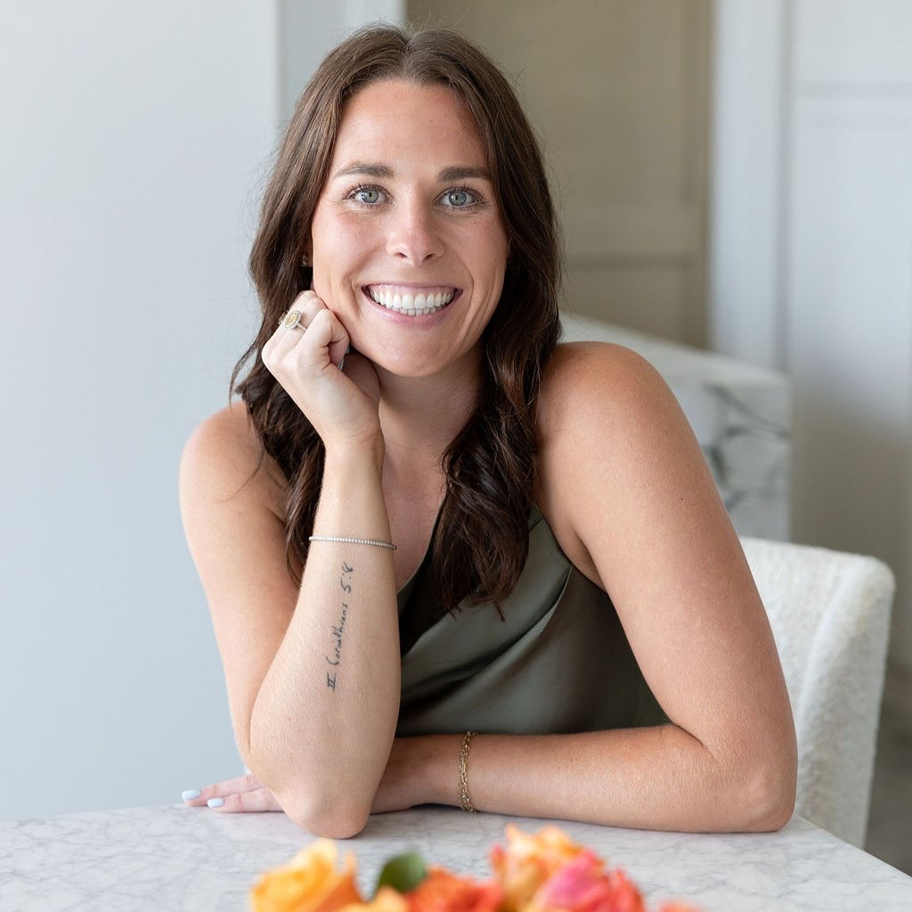 Lindsey McDowell Rice seated at a marble table, smiling with her chin resting on one hand.