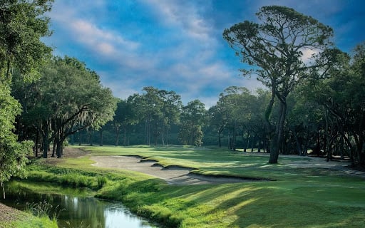 Golf course with rolling fairways, mature trees, and a water hazard.
