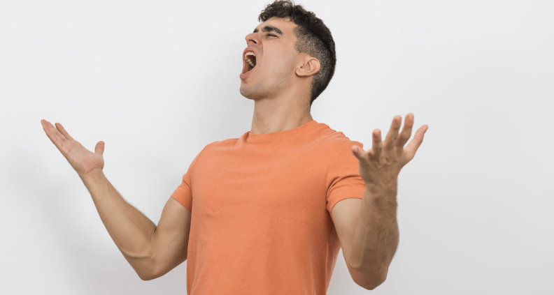Man in an orange T-shirt shouting with his arms raised