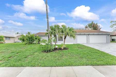Single-story home with a two-car garage, broad front lawn, and small palm tree.