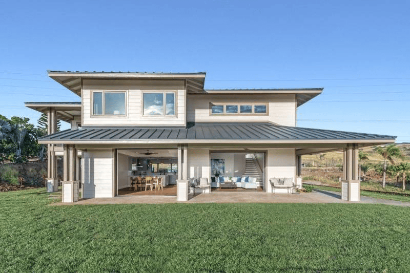 Two-story modern home with a dark metal roof, covered patio, and broad green lawn.