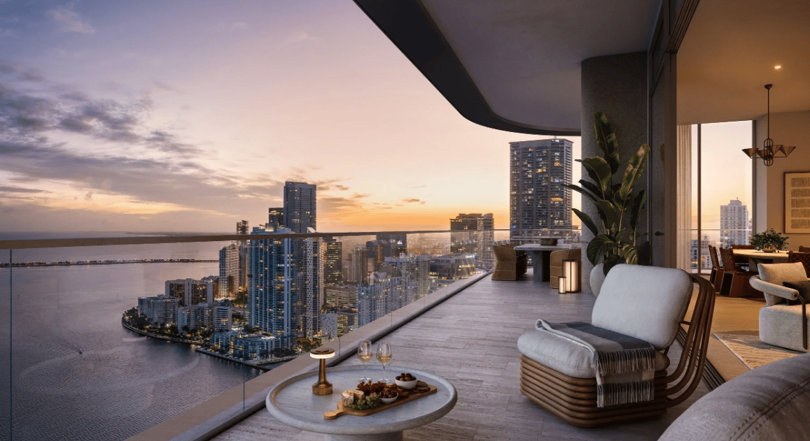 Luxury condo balcony overlooking Brickell Key’s waterfront skyline at sunset, with lounge seating and an adjoining dining area.