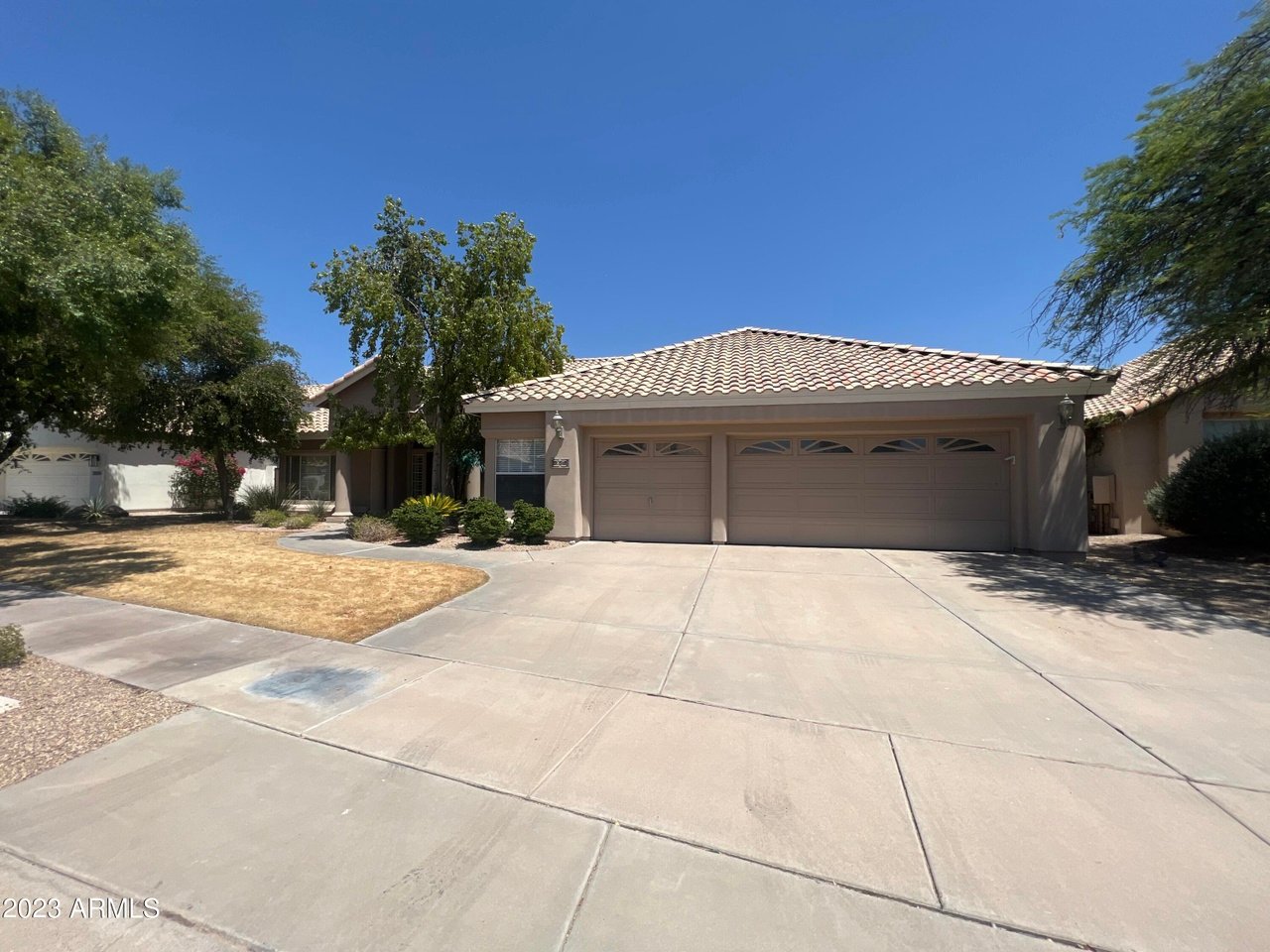 Single-story stucco home with a tile roof, three-car garage, and wide concrete driveway.