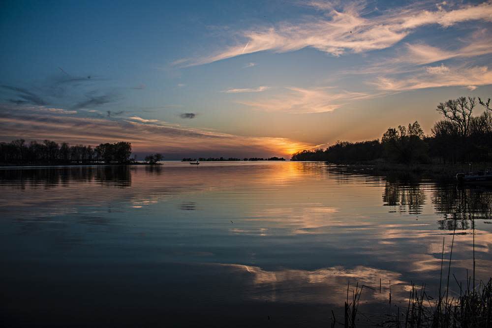 Sunset over a calm lake, reflected in the water between tree-lined shores.