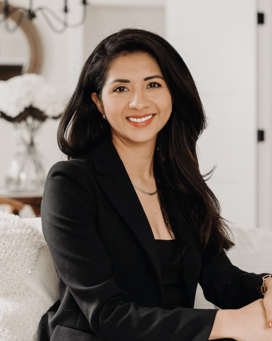 Faride Cuevas Ayala seated indoors, smiling in a black blazer.