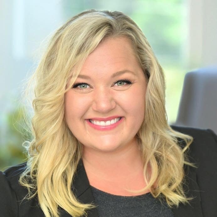 Kristen Cowan smiling in a black blazer, with long blonde hair.