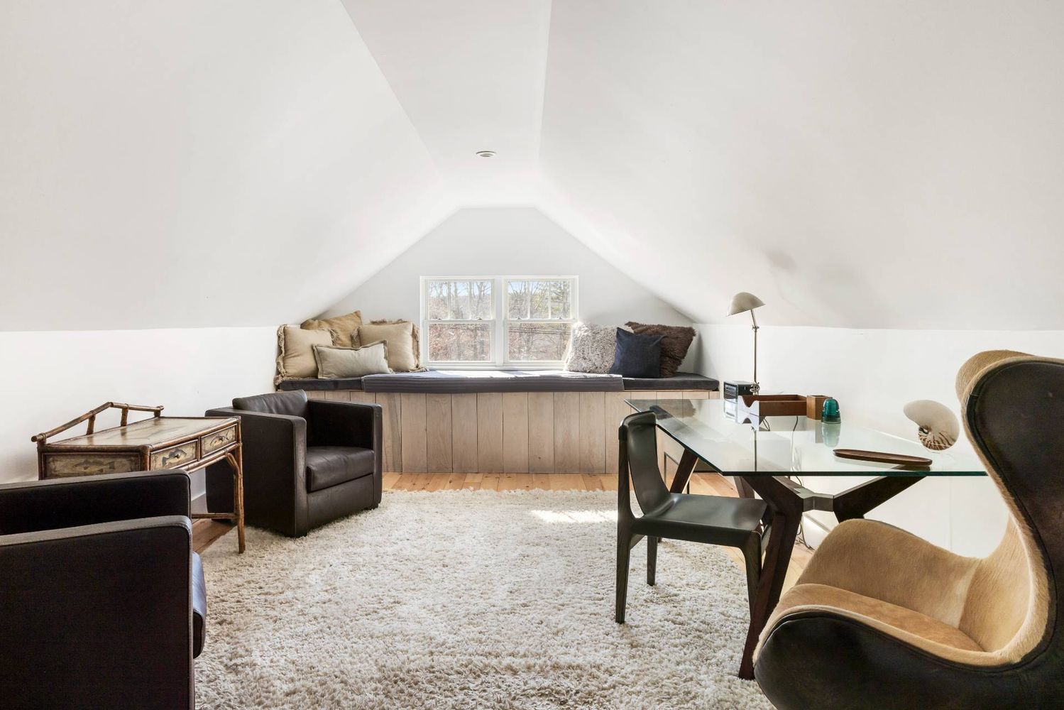Attic sitting room with a window seat, sloped ceiling, leather chairs, and glass-top table.