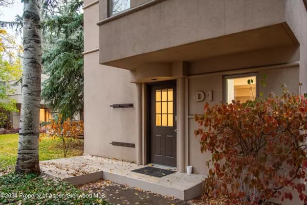 Stucco building entrance marked D1, with a dark paneled door and autumn foliage.