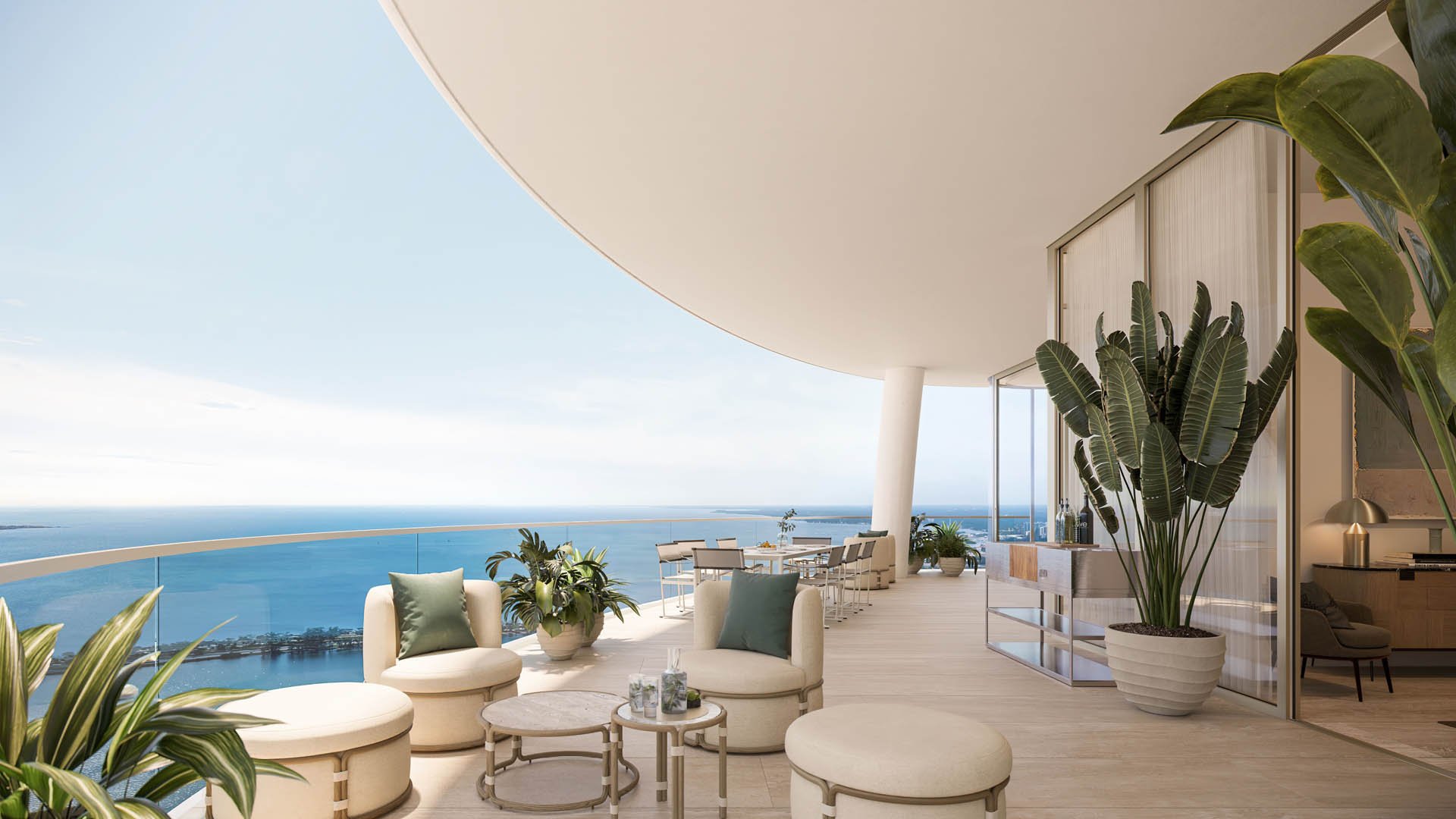 Furnished terrace overlooking the ocean, with curved glass railing, lounge seating, and tropical plants.