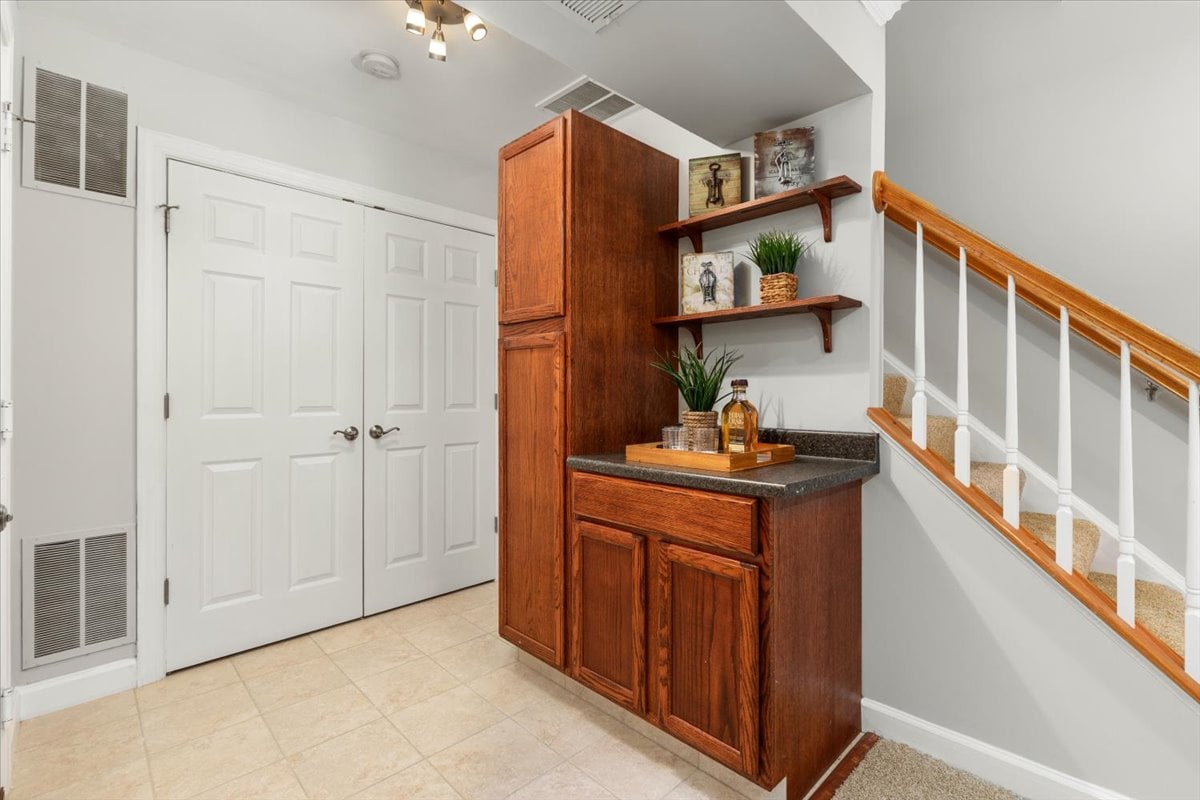 Entryway with wooden cabinetry and display shelves beside white double doors and a carpeted staircase.