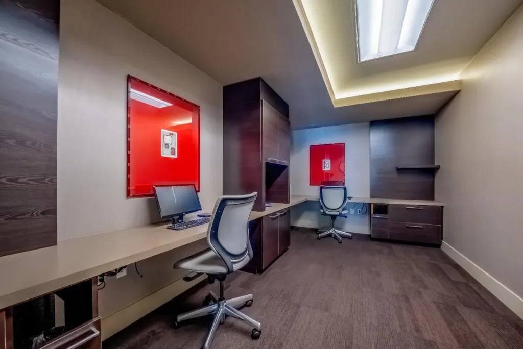 Stylish home office workspace at Madrone featuring built-in desk, ergonomic chair, red accent lighting, dark wood cabinetry, and modern storage solutions