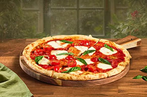 Margherita pizza with fresh basil on a wooden board beside a green cloth.