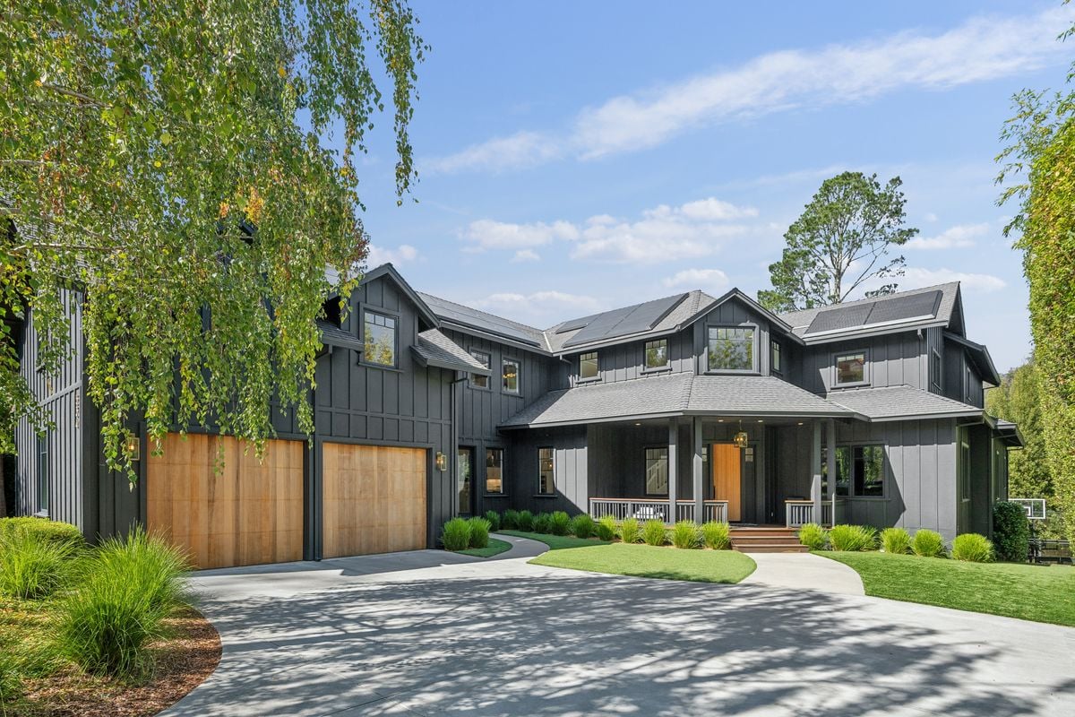 Modern dark-sided home with solar panels, wood garage doors, and a landscaped front lawn.